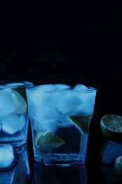 Photo of Shot glasses of vodka with ice cubes and lime slices on dark background