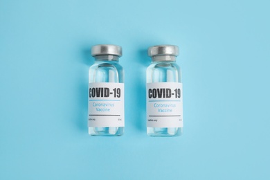 Photo of Vials with coronavirus vaccine on light blue background, flat lay