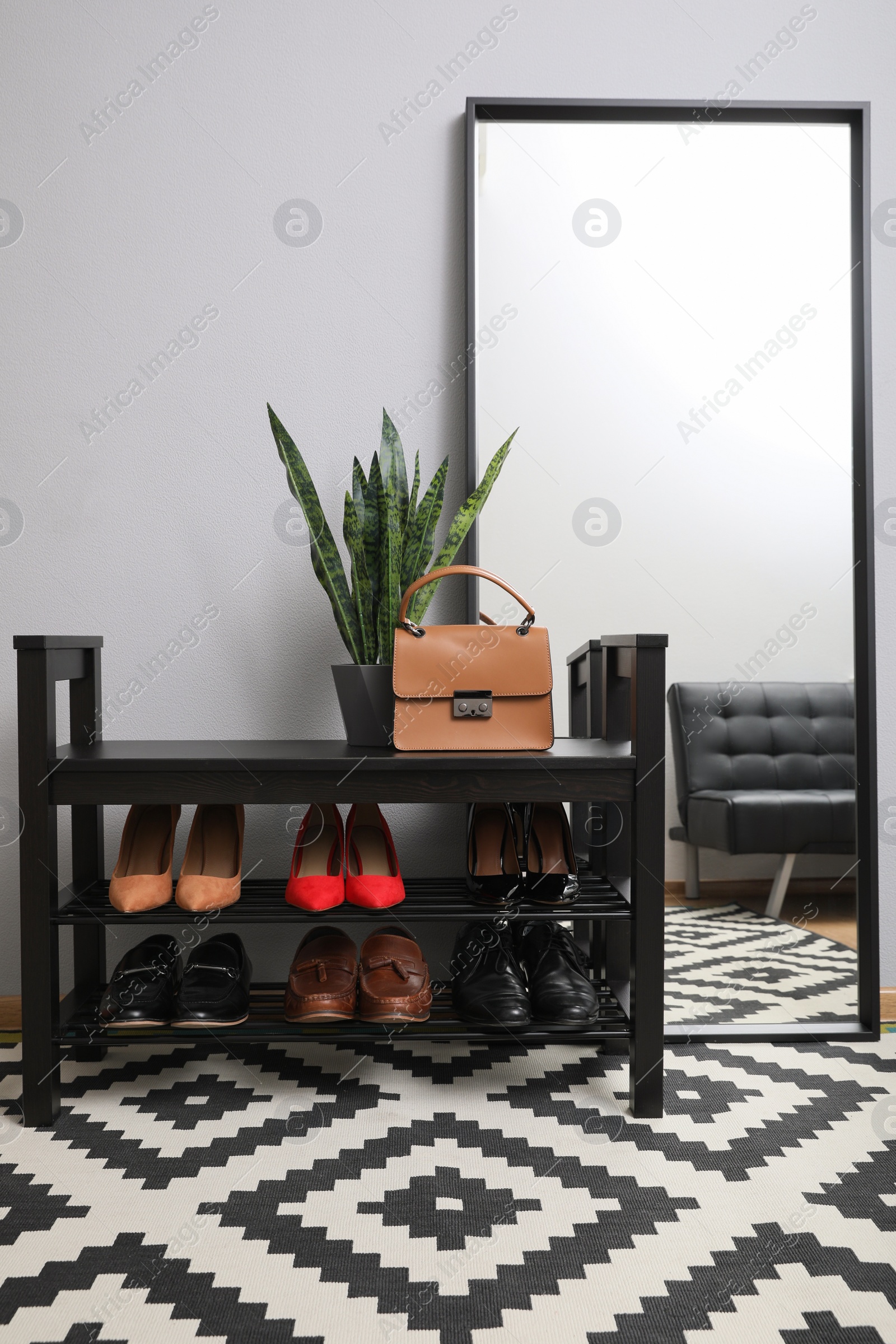 Photo of Shelving unit with stylish shoes and large mirror near grey wall in hallway