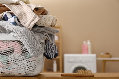 Photo of Laundry basket with baby clothes and hairbrush on wooden table in bathroom. Space for text