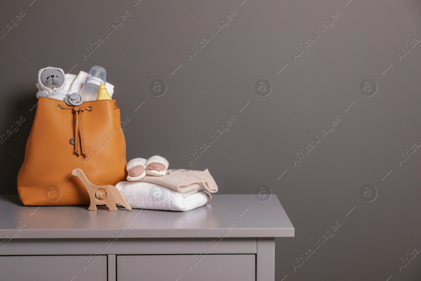 Photo of Mother's bag with baby's stuff on commode near gray wall, space for text