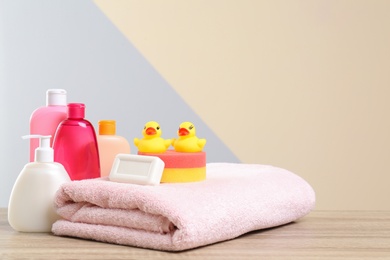 Photo of Baby cosmetic products, toys and towel on table against color background. Space for text