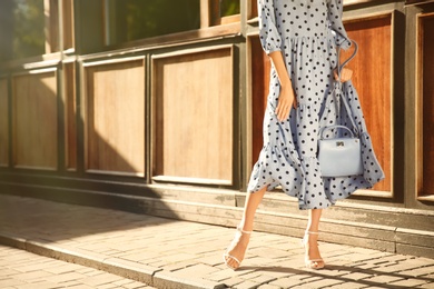 Photo of Woman in stylish light blue polka dot dress and high heel shoes with handbag on city street, closeup