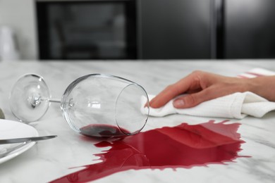 Woman cleaning spilled wine on white marble table in kitchen, closeup