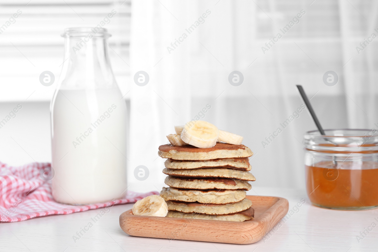 Photo of Plate of banana pancakes with honey and milk on white wooden table
