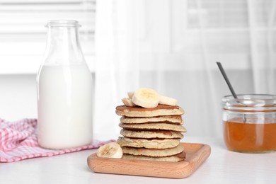 Plate of banana pancakes with honey and milk on white wooden table