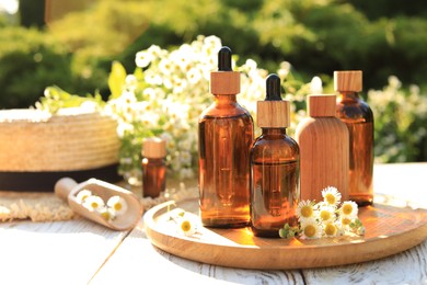Photo of Bottles of essential oil and flowers on white wooden table outdoors, space for text