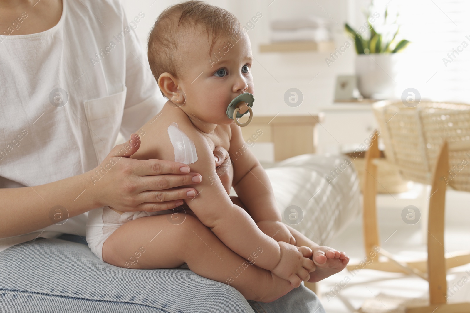 Photo of Mother applying body cream on her little baby at home, closeup