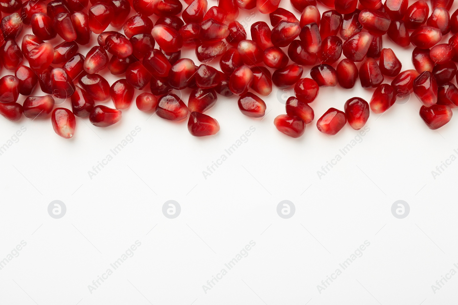 Photo of Many ripe juicy pomegranate grains on white background, flat lay. Space for text