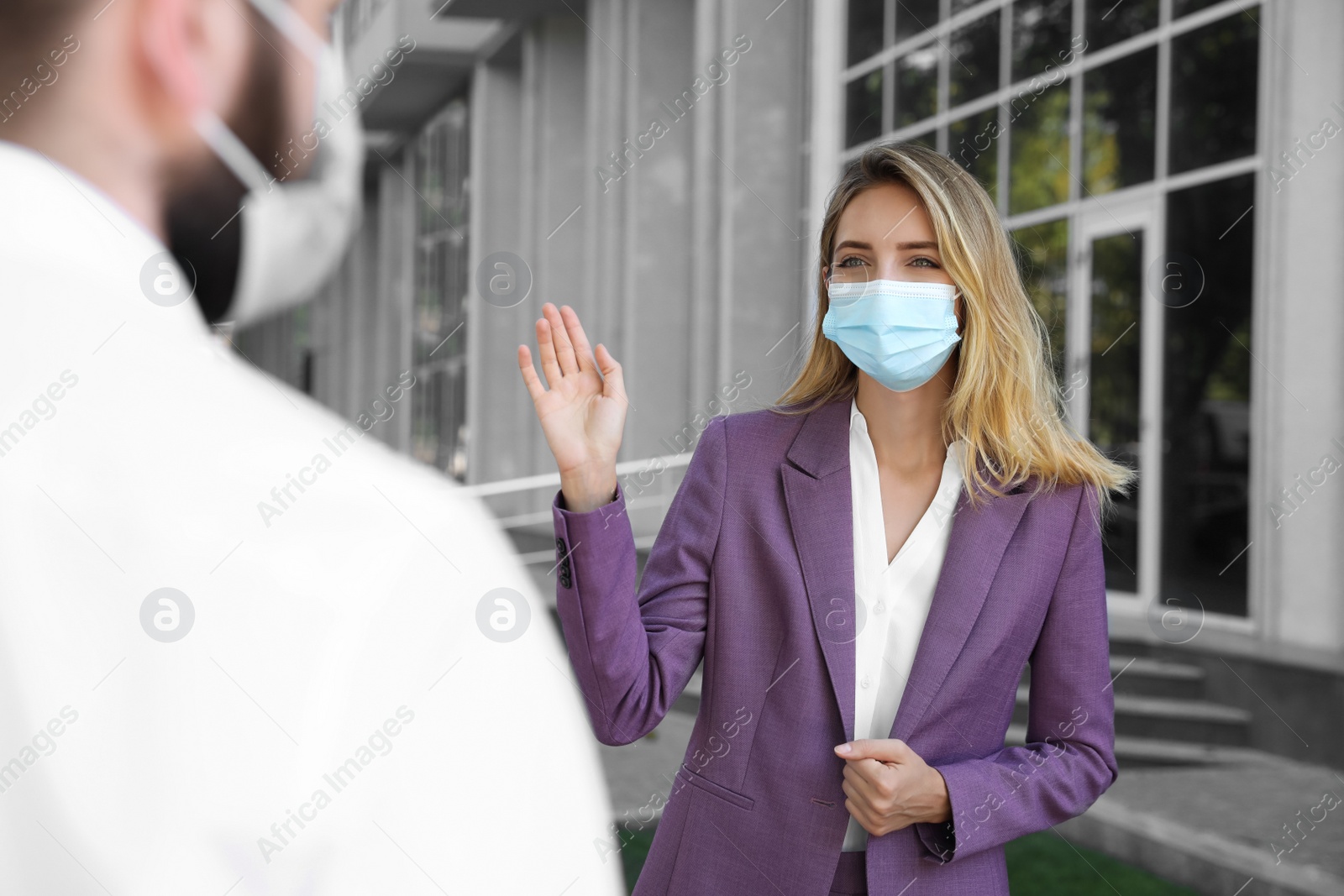 Photo of Woman in protective face mask saying hello outdoors. Keeping social distance during coronavirus pandemic