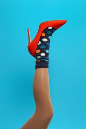 Photo of Woman wearing sock and high heel shoe on light blue background, closeup