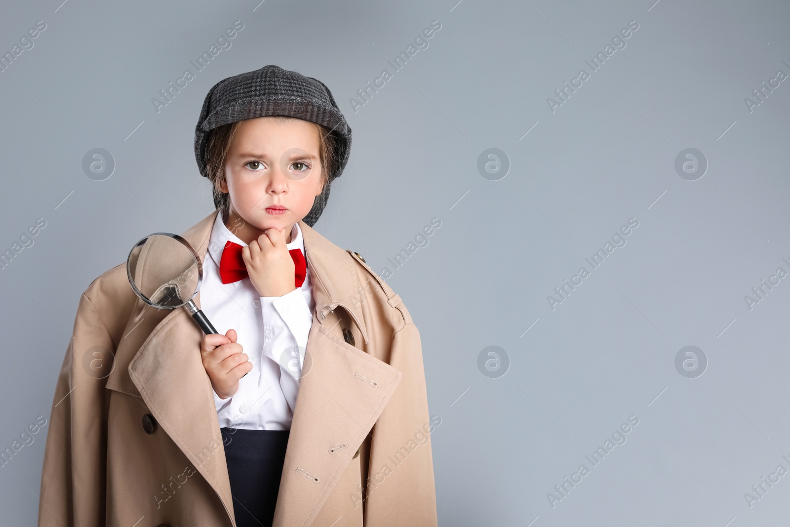 Photo of Cute little child in hat with magnifying glass playing detective on grey background, space for text