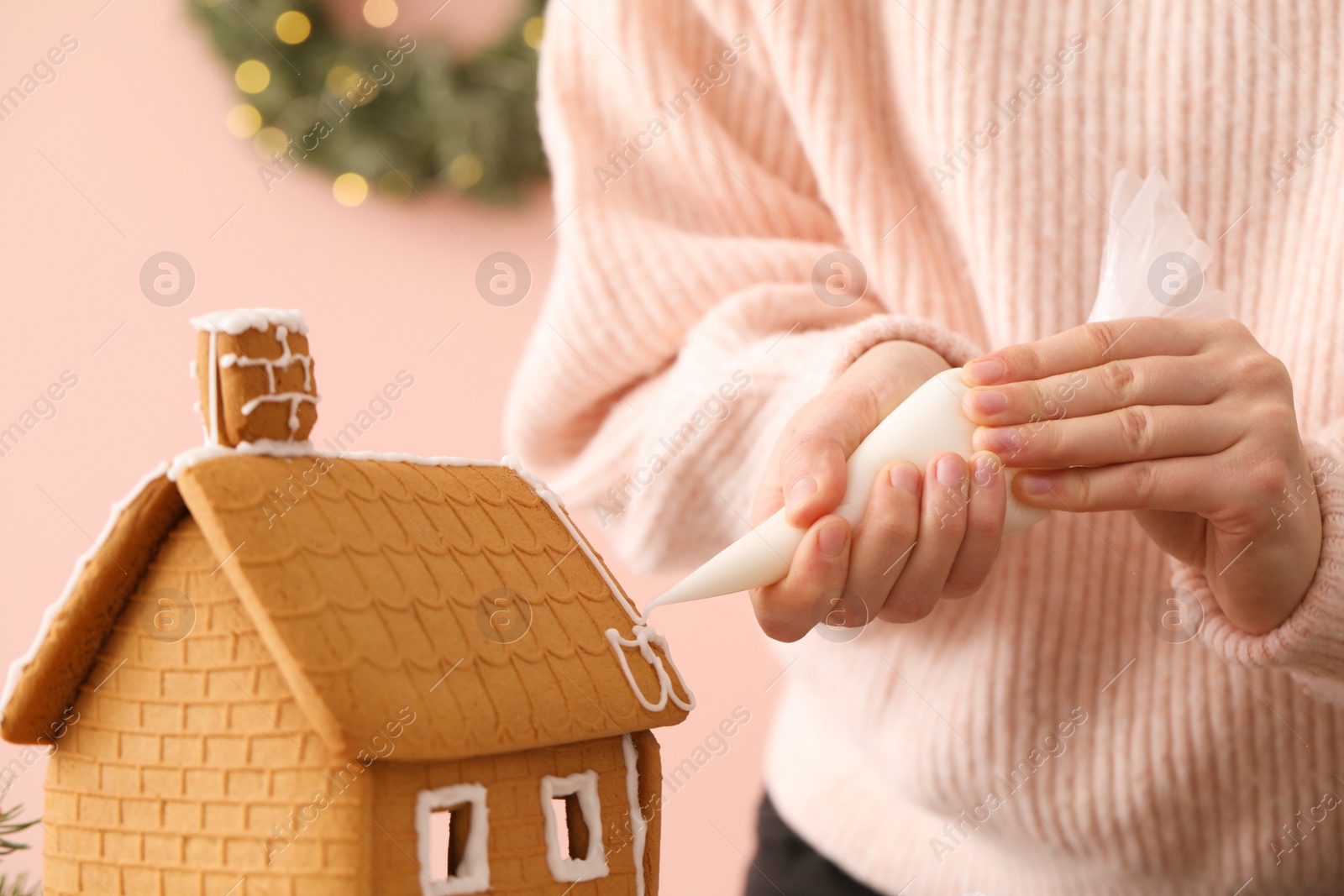 Photo of Woman decorating gingerbread house with icing on pink background, closeup