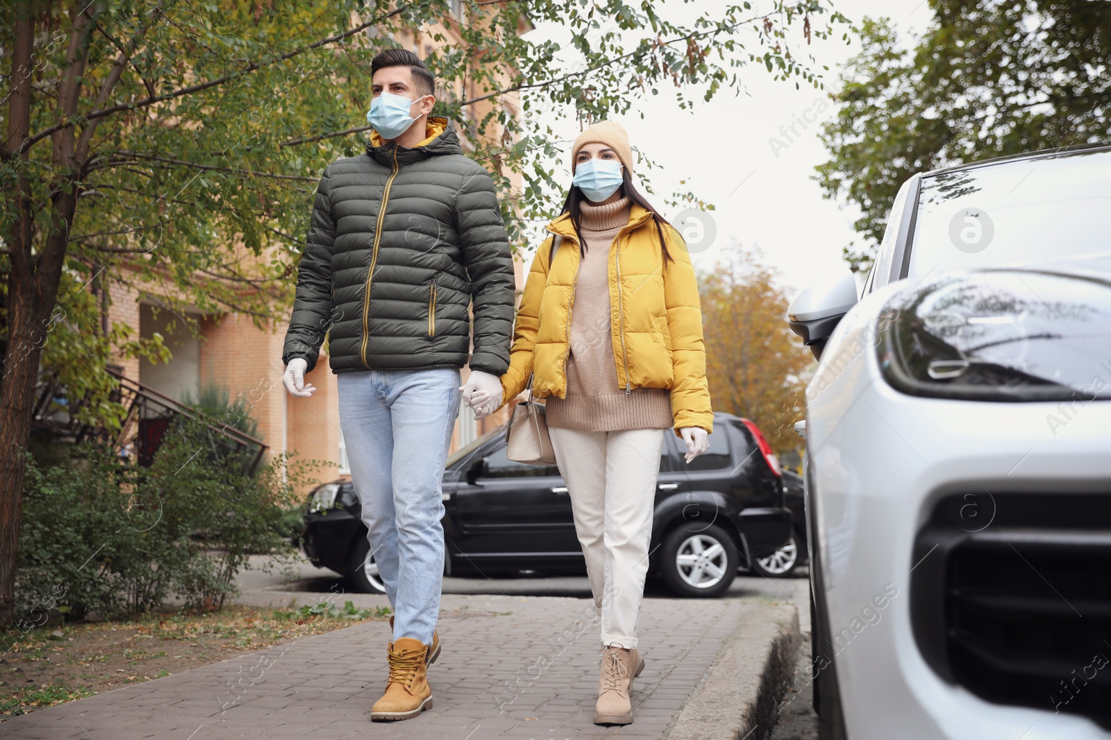 Photo of Couple in medical face masks and gloves walking outdoors. Personal protection during COVID-19 pandemic