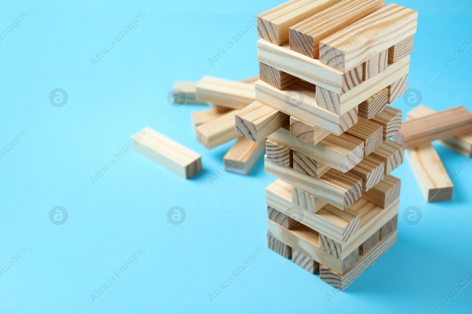 Photo of Jenga tower and wooden blocks on light blue background, space for text