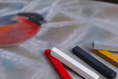 Photo of Colorful chalk pastels on beautiful painting of bullfinch, closeup