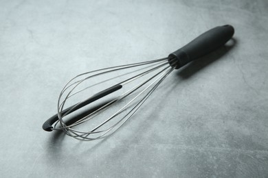 Photo of Metal whisk on gray table, closeup. Kitchen tool