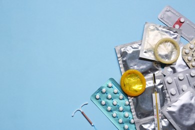 Contraceptive pills, condoms, intrauterine device and thermometer on light blue background, flat lay with space for text. Different birth control methods