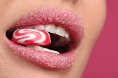 Young woman with beautiful lips covered in sugar eating candy on pink background, closeup
