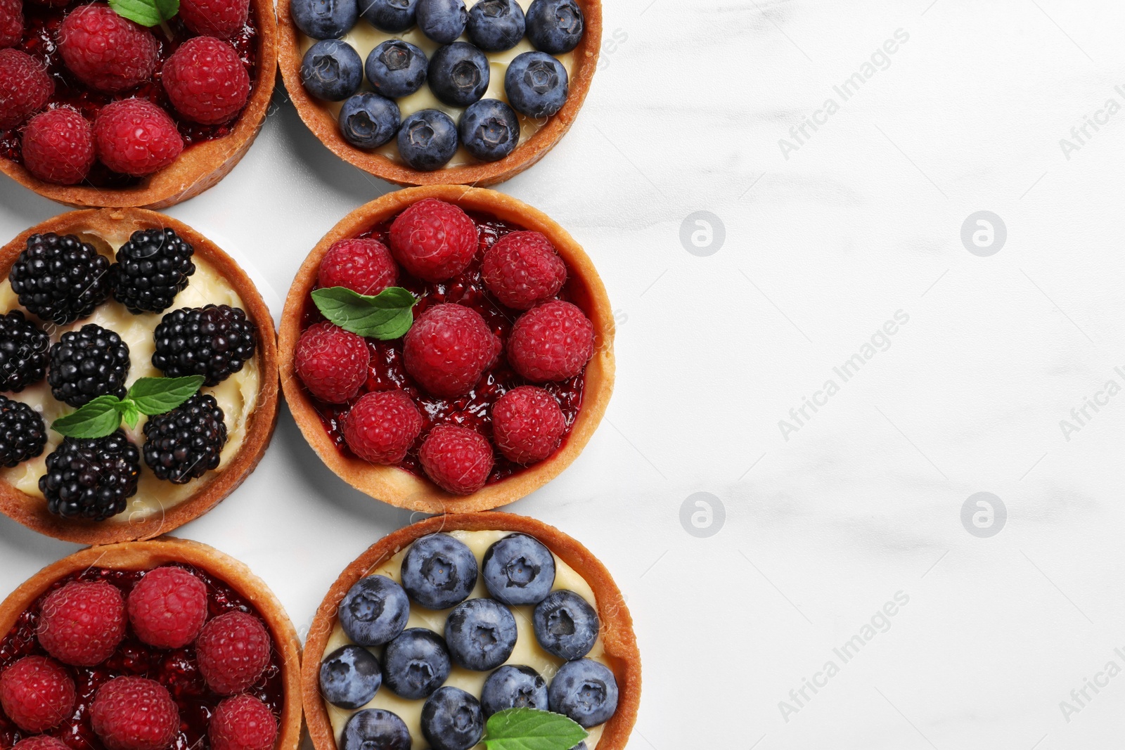 Photo of Tartlets with different fresh berries on white marble table, flat lay and space for text. Delicious dessert