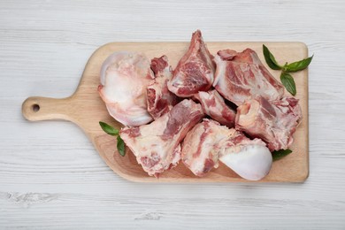 Cutting board with raw chopped meaty bones and basil on white wooden table, top view