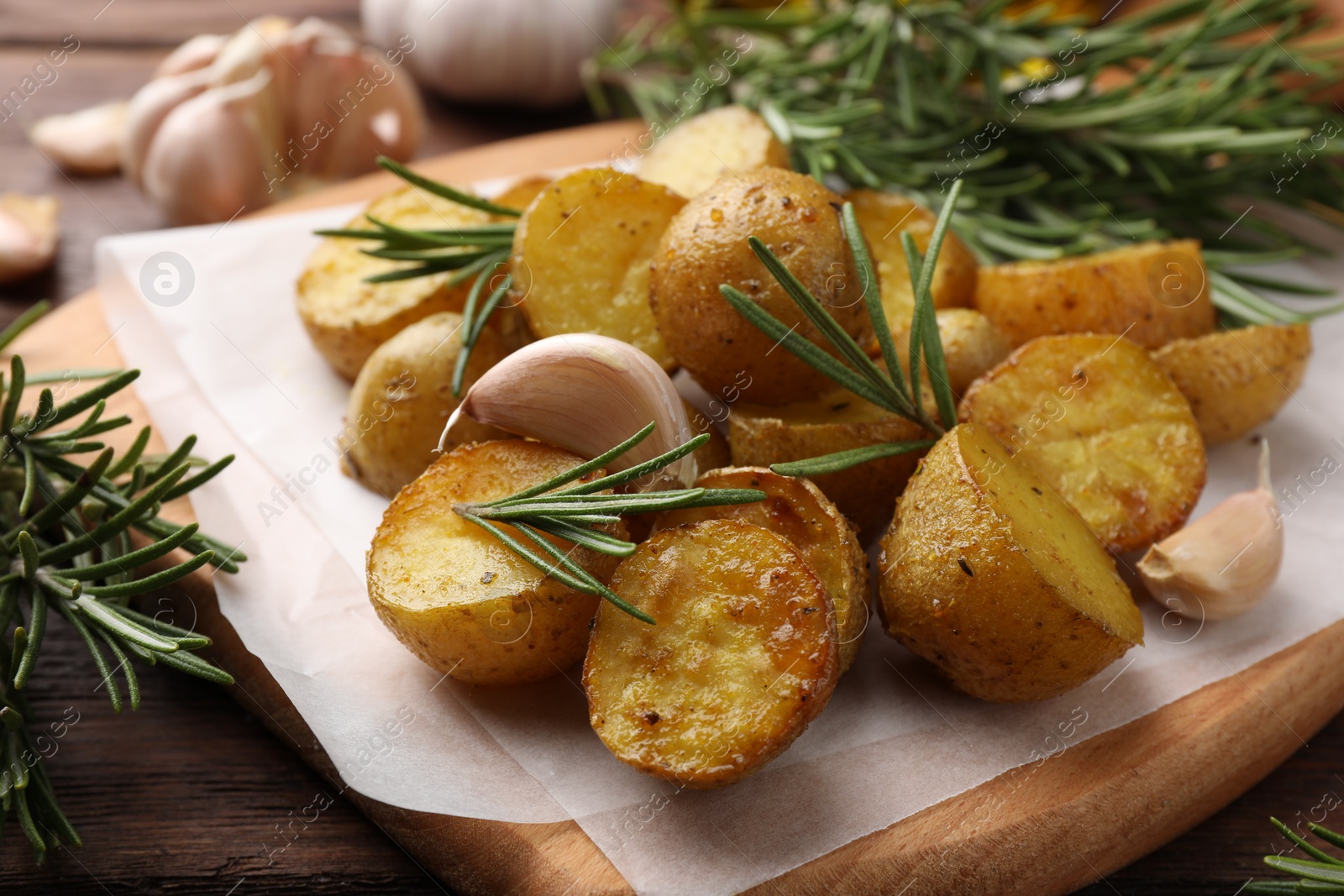 Photo of Delicious baked potatoes with rosemary and garlic on parchment paper, closeup