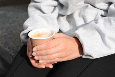 Photo of Woman sitting with cardboard cup of coffee outdoors, closeup