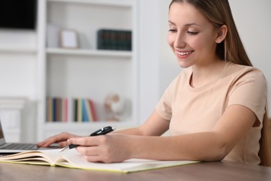 Photo of Online learning. Teenage girl writing in notebook near laptop at home