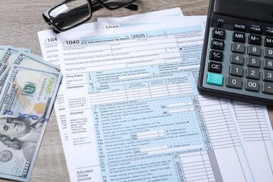 Photo of Payroll. Tax return forms, dollar banknotes, glasses and calculator on wooden table