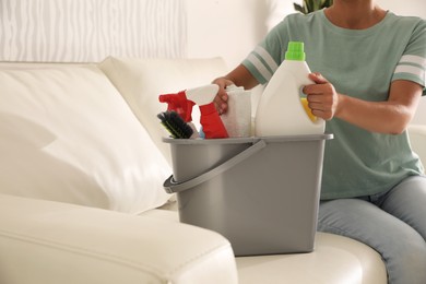 Photo of Woman holding bucket with cleaning supplies in living room, closeup