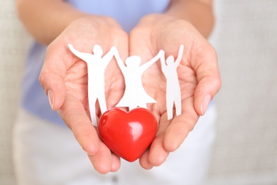 Photo of Young woman holding paper family figure and red heart, closeup of hands