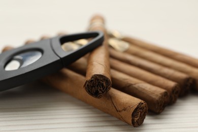 Photo of Cigars and guillotine cutter on white wooden table, closeup