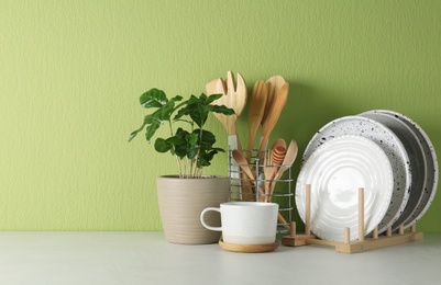 Photo of Potted plant and set of kitchenware on white table near green wall, space for text. Modern interior design