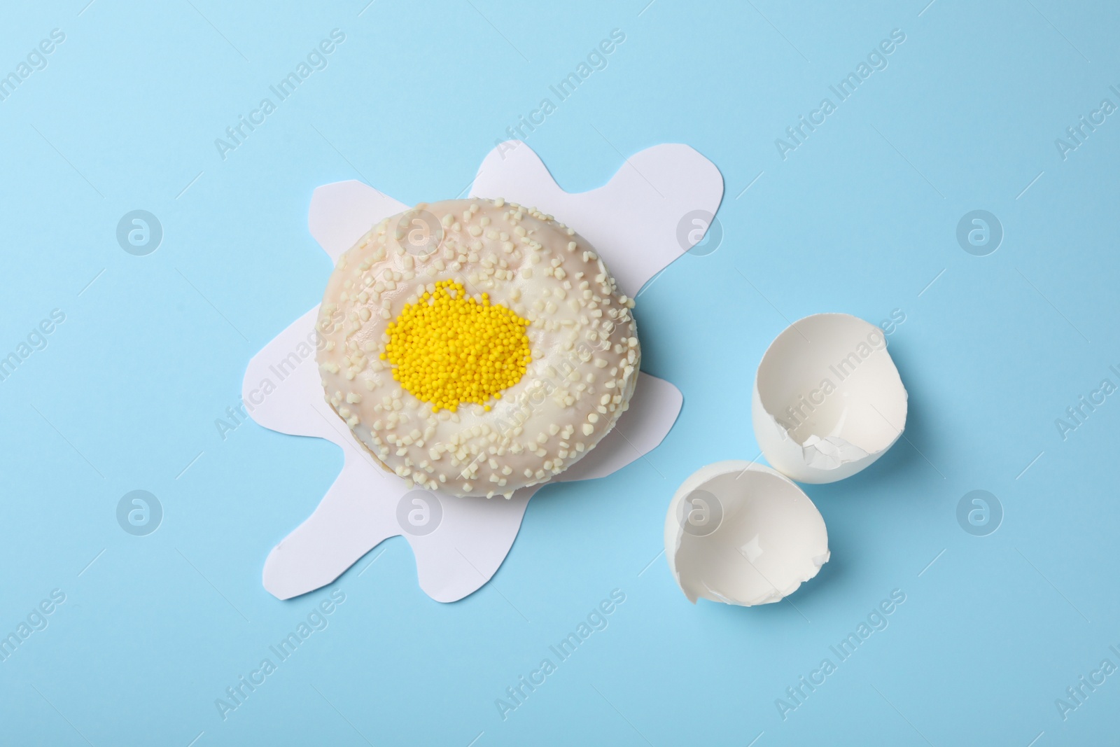 Photo of Broken egg made with donut and paper on light blue background, flat lay