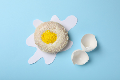 Broken egg made with donut and paper on light blue background, flat lay