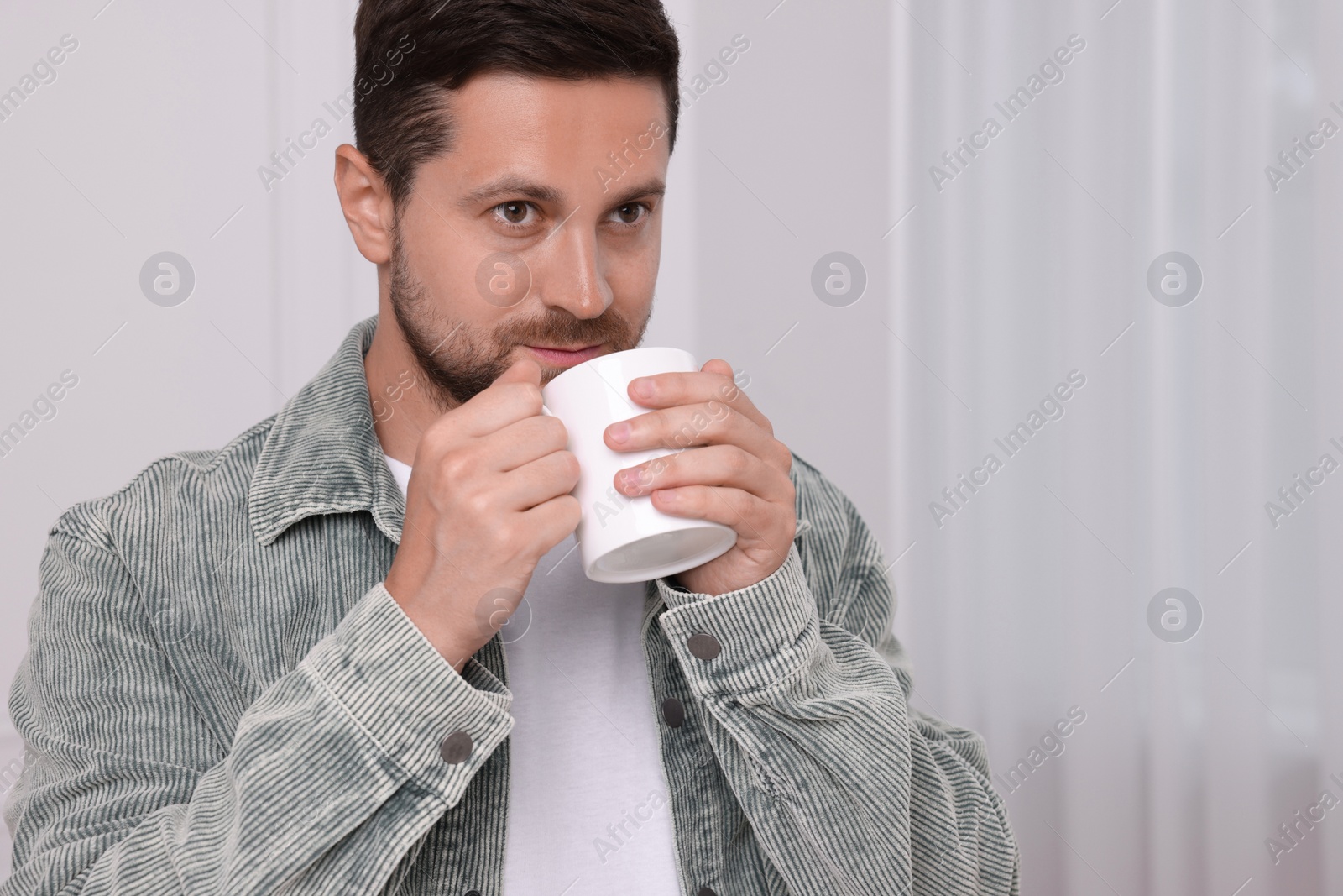 Photo of Man drinking from white mug at home. Space for text