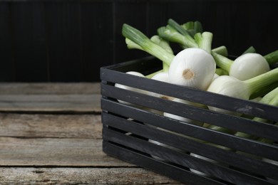 Photo of Black crate with green spring onions on wooden table, closeup. Space for text