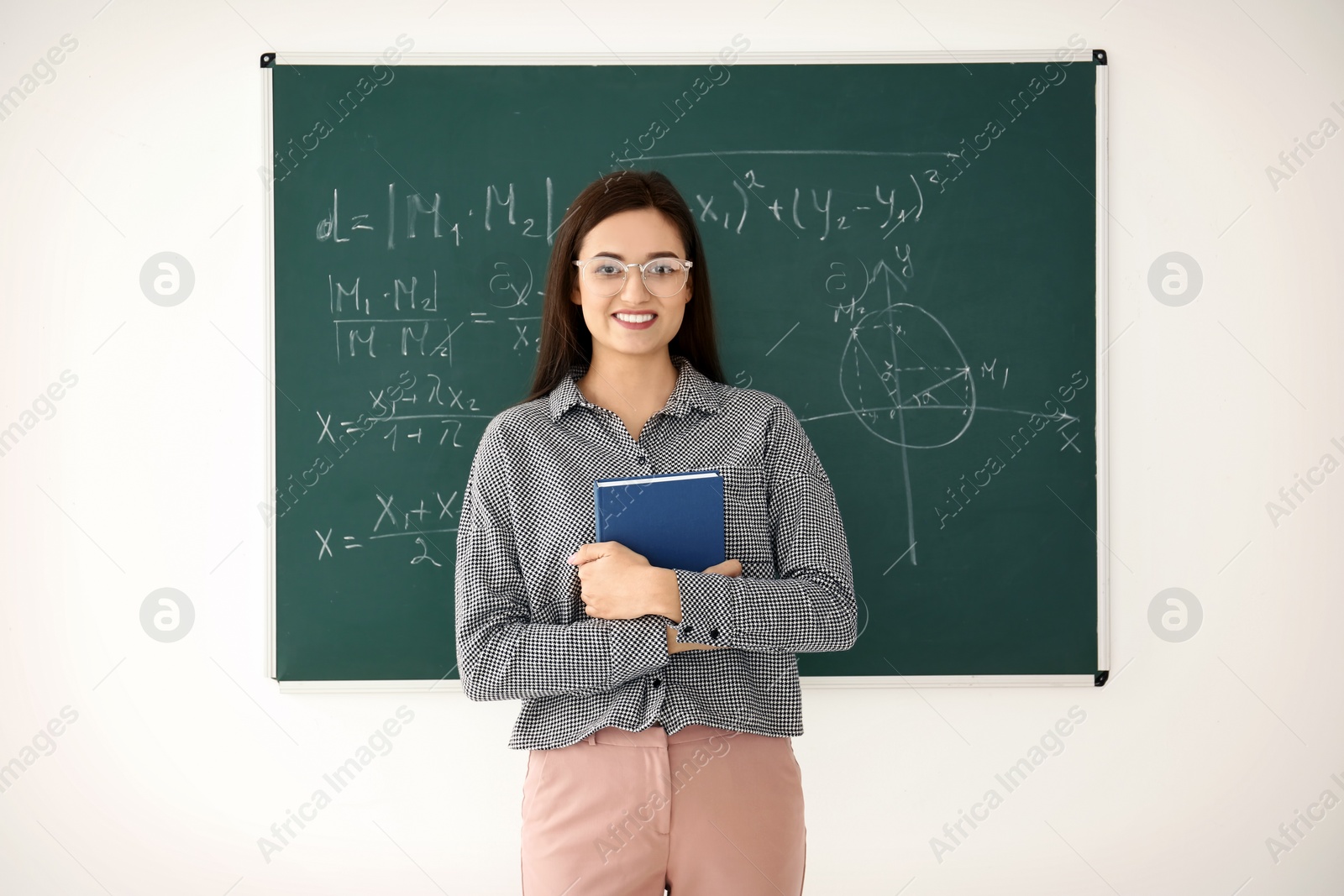 Photo of Female teacher with book standing near blackboard in classroom