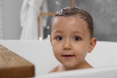 Photo of Cute little boy washing hair with shampoo in bathroom