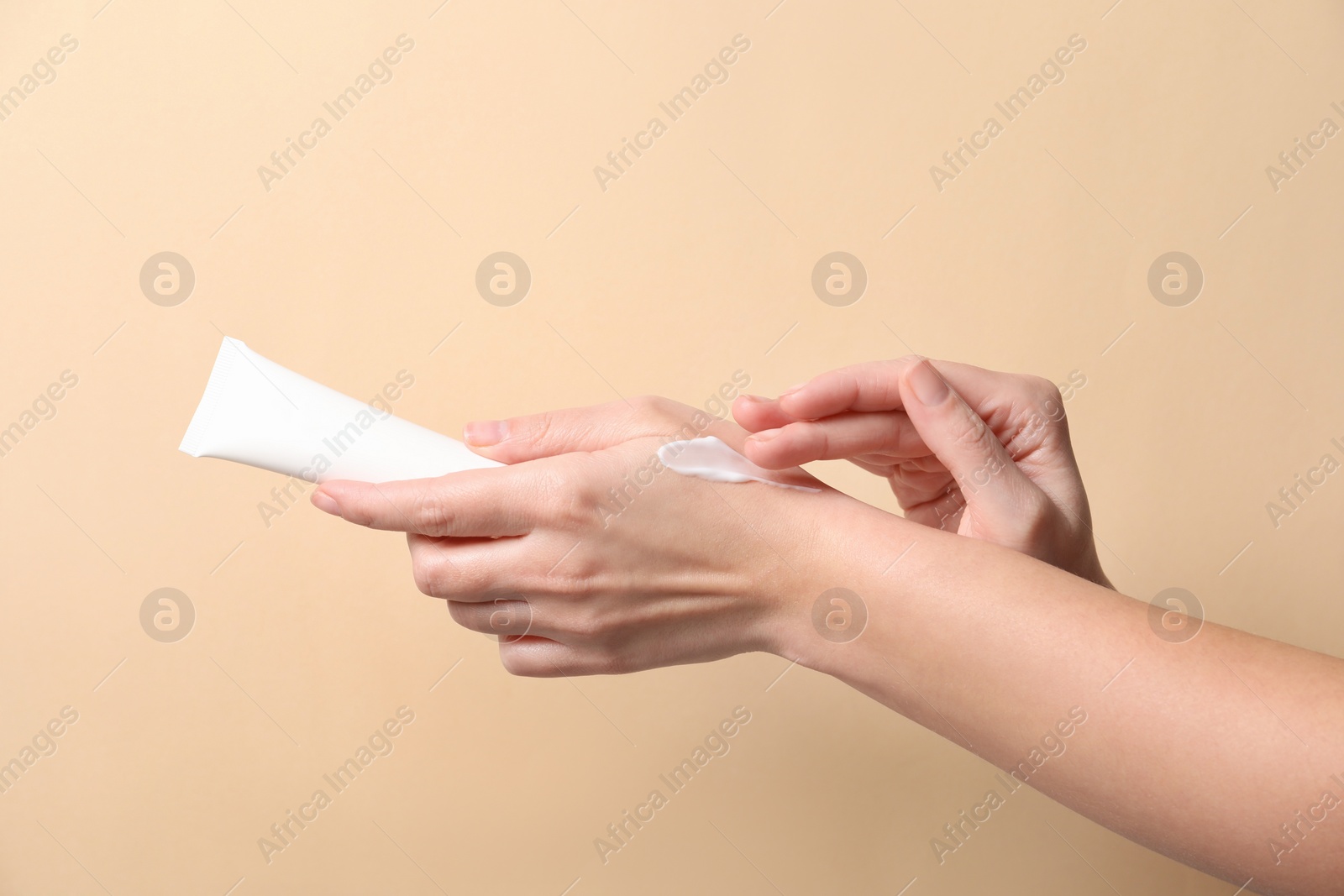 Photo of Woman with tube applying cosmetic cream onto her hand on beige background, closeup