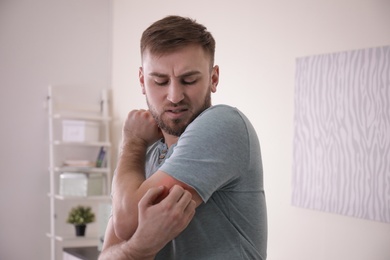 Photo of Young man scratching arm indoors. Allergy symptoms
