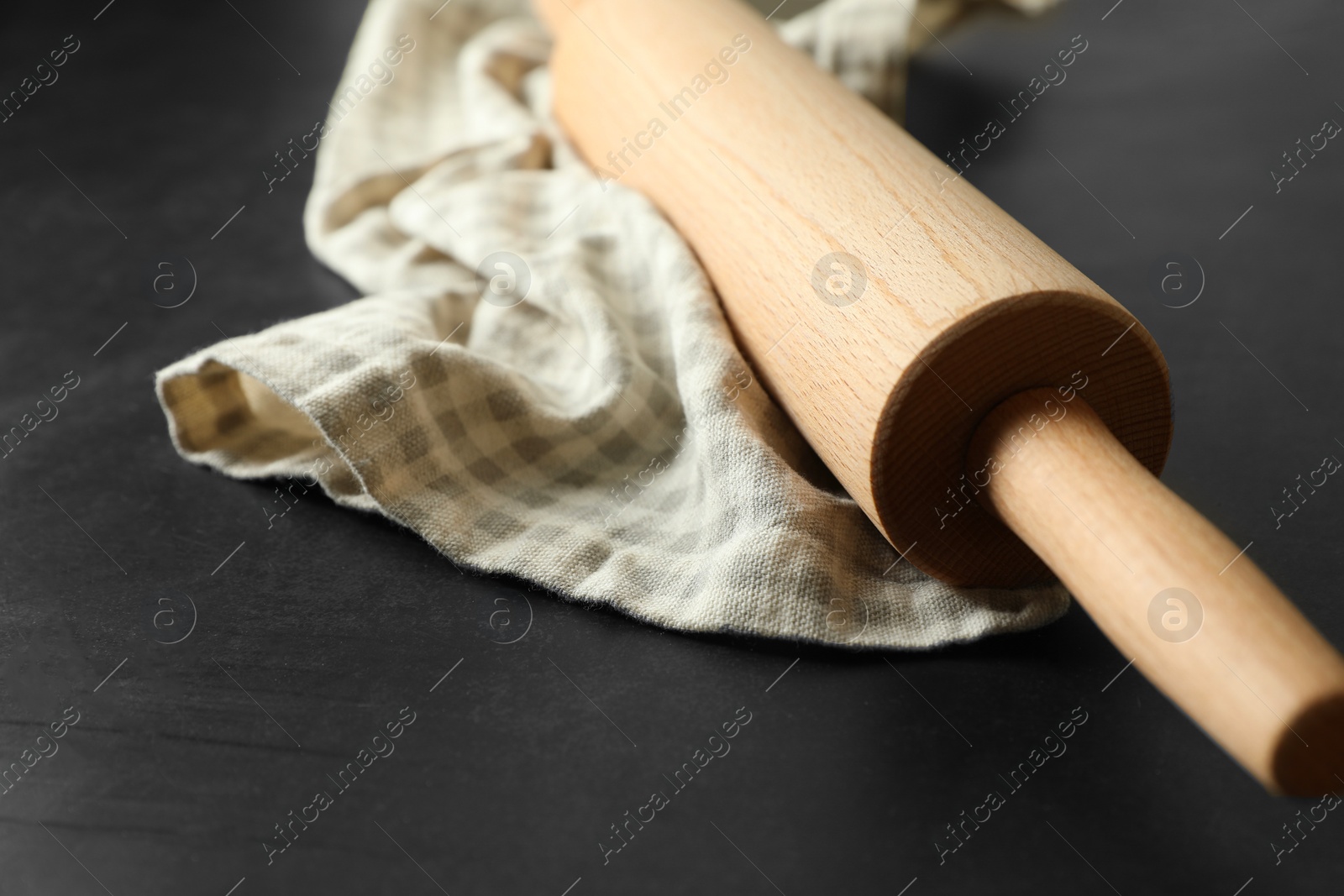 Photo of Rolling pin and kitchen towel on black table, closeup