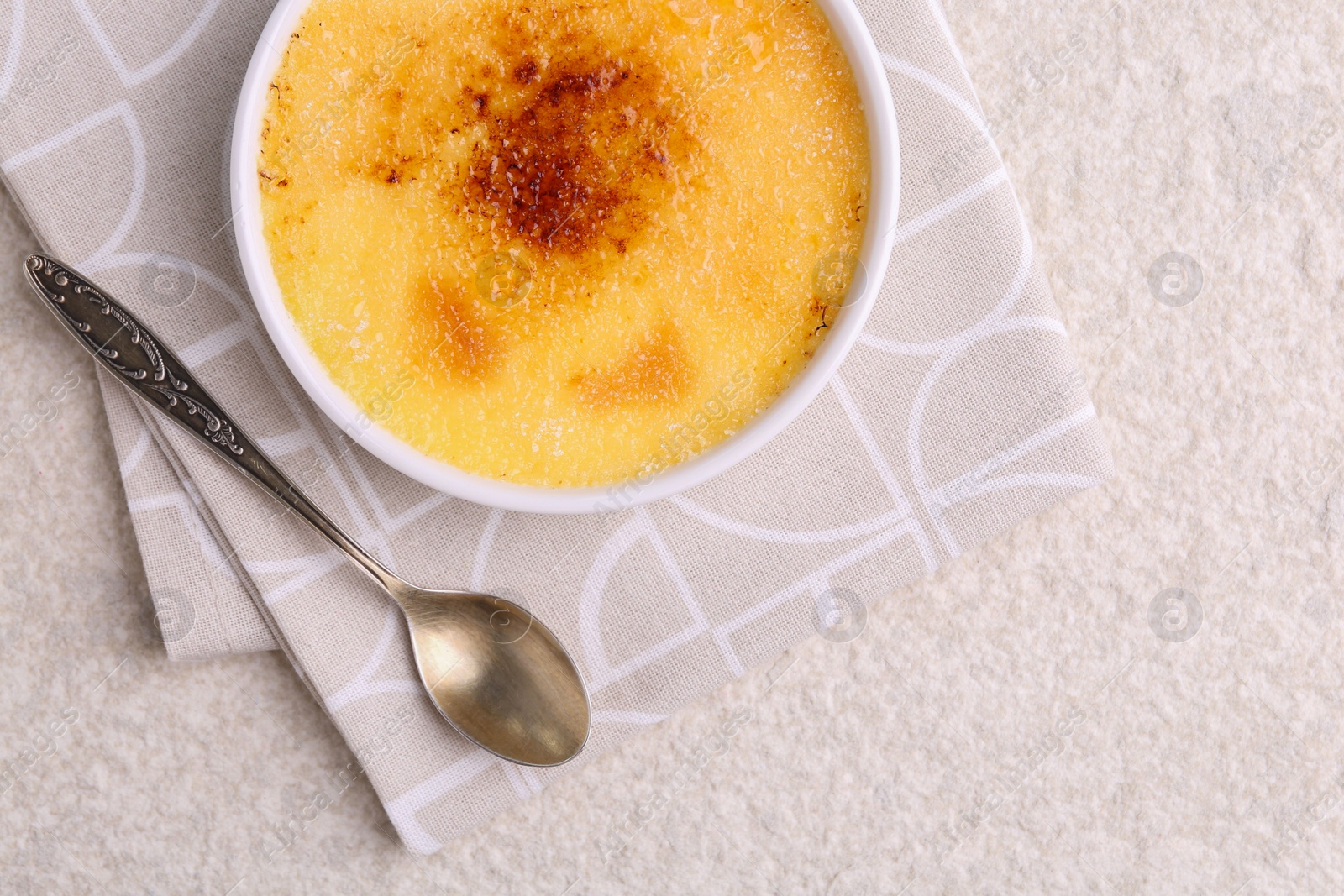 Photo of Delicious creme brulee in bowl and spoon on light textured table, top view. Space for text