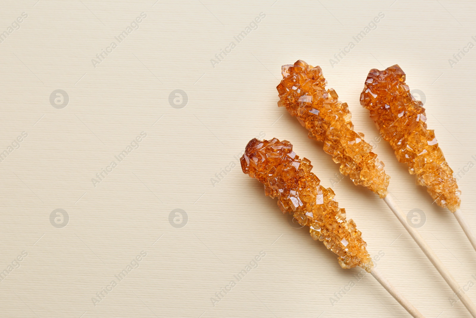 Photo of Wooden sticks with sugar crystals and space for text on beige background, flat lay. Tasty rock candies