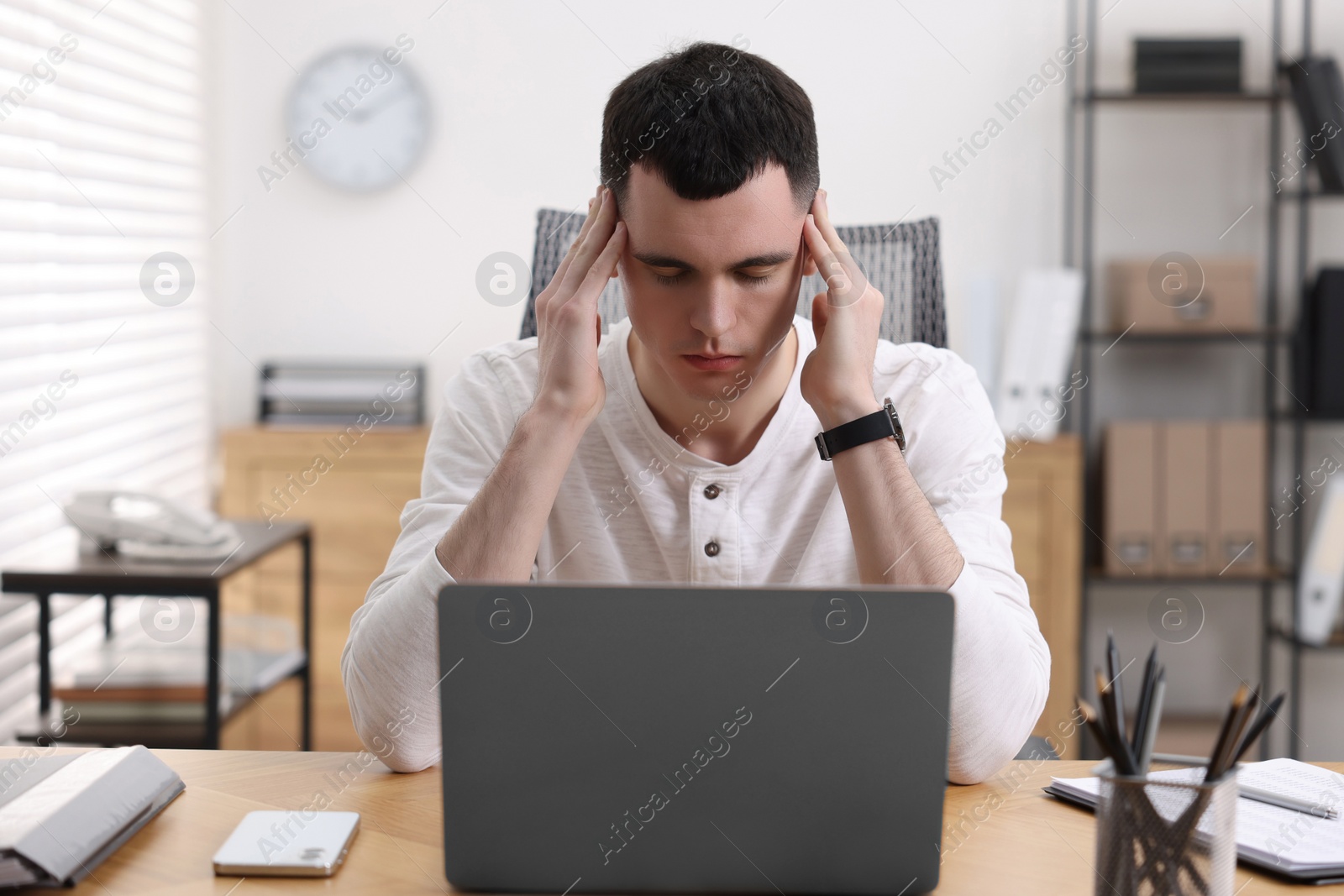 Photo of Young man suffering from headache at workplace in office