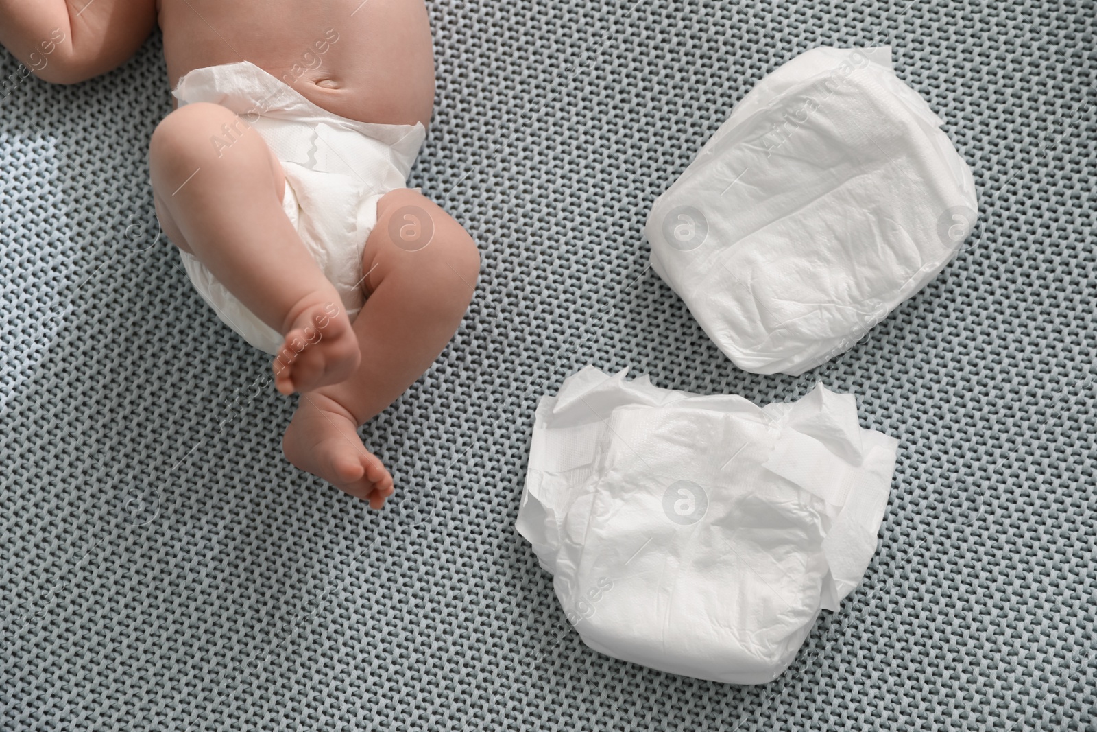 Photo of Cute little baby in diaper lying on bed, top view