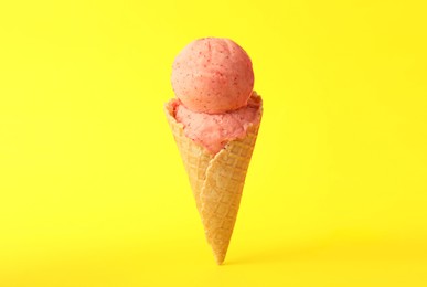 Photo of Delicious pink ice cream in waffle cone on yellow background