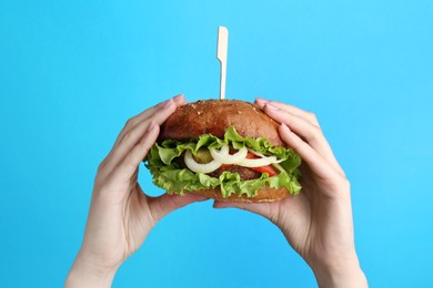 Woman holding delicious vegetarian burger on light blue background, closeup