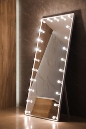 Modern mirror with light bulbs near brown wall in room