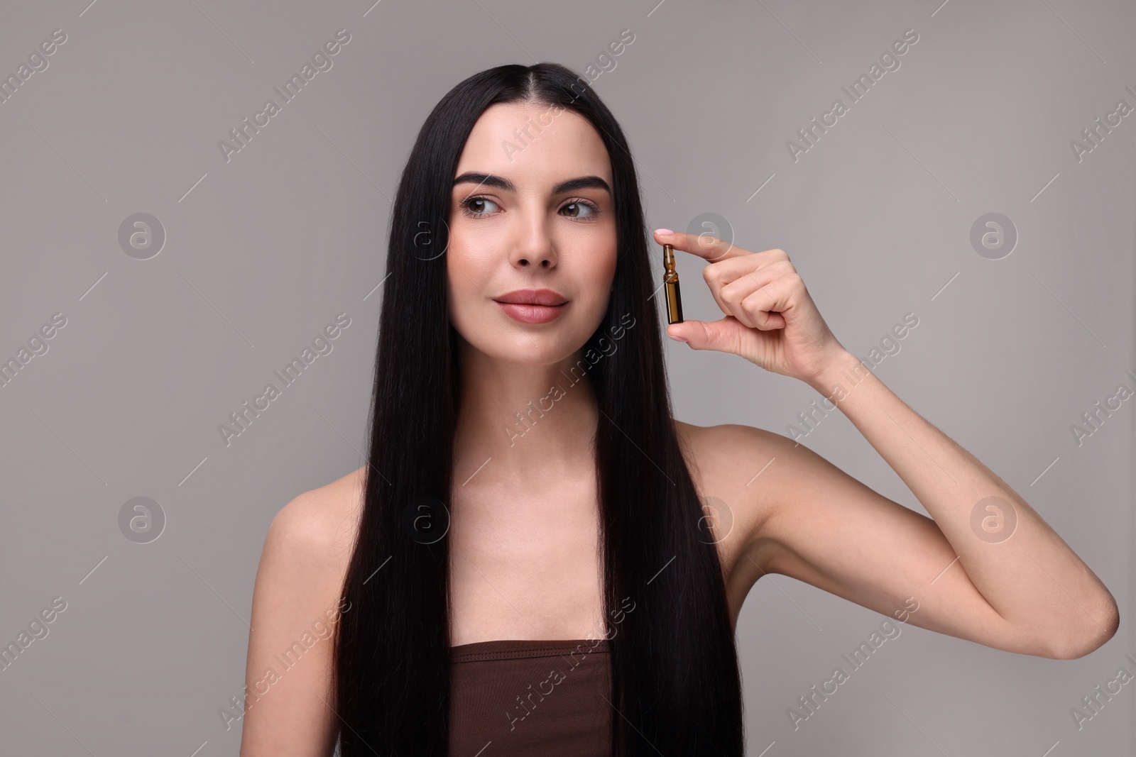 Photo of Beautiful young woman holding skincare ampoule on grey background